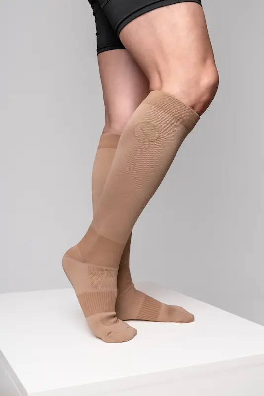 Stridely warm neutral tan compression socks photographed on white studio pedestal