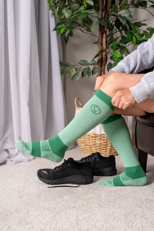 Pulling on Stridely sage green compression socks with running shoes